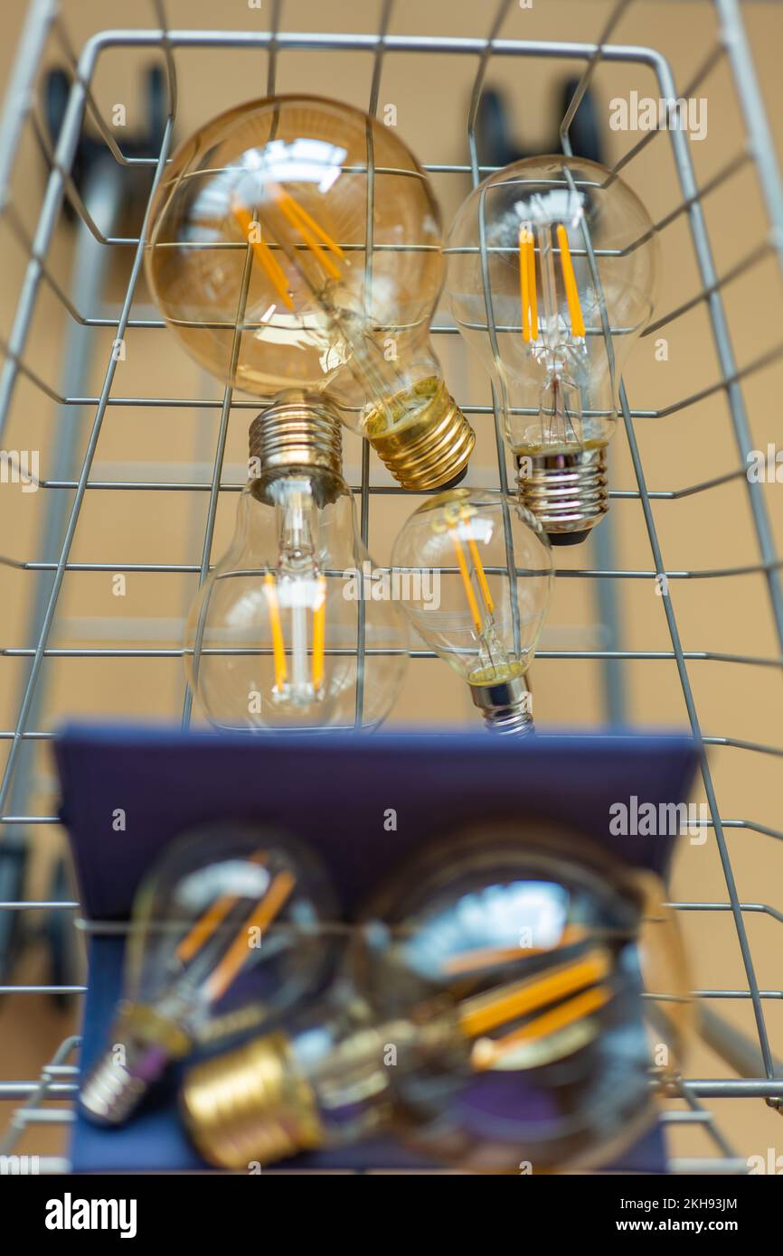 Kauf von Elektrizität. Viele elektrische Lampen in einem Einkaufswagen. Verbrauch und Bezahlung für Energieverbrauch. Glühbirnen in einem Wagen in Beige Stockfoto