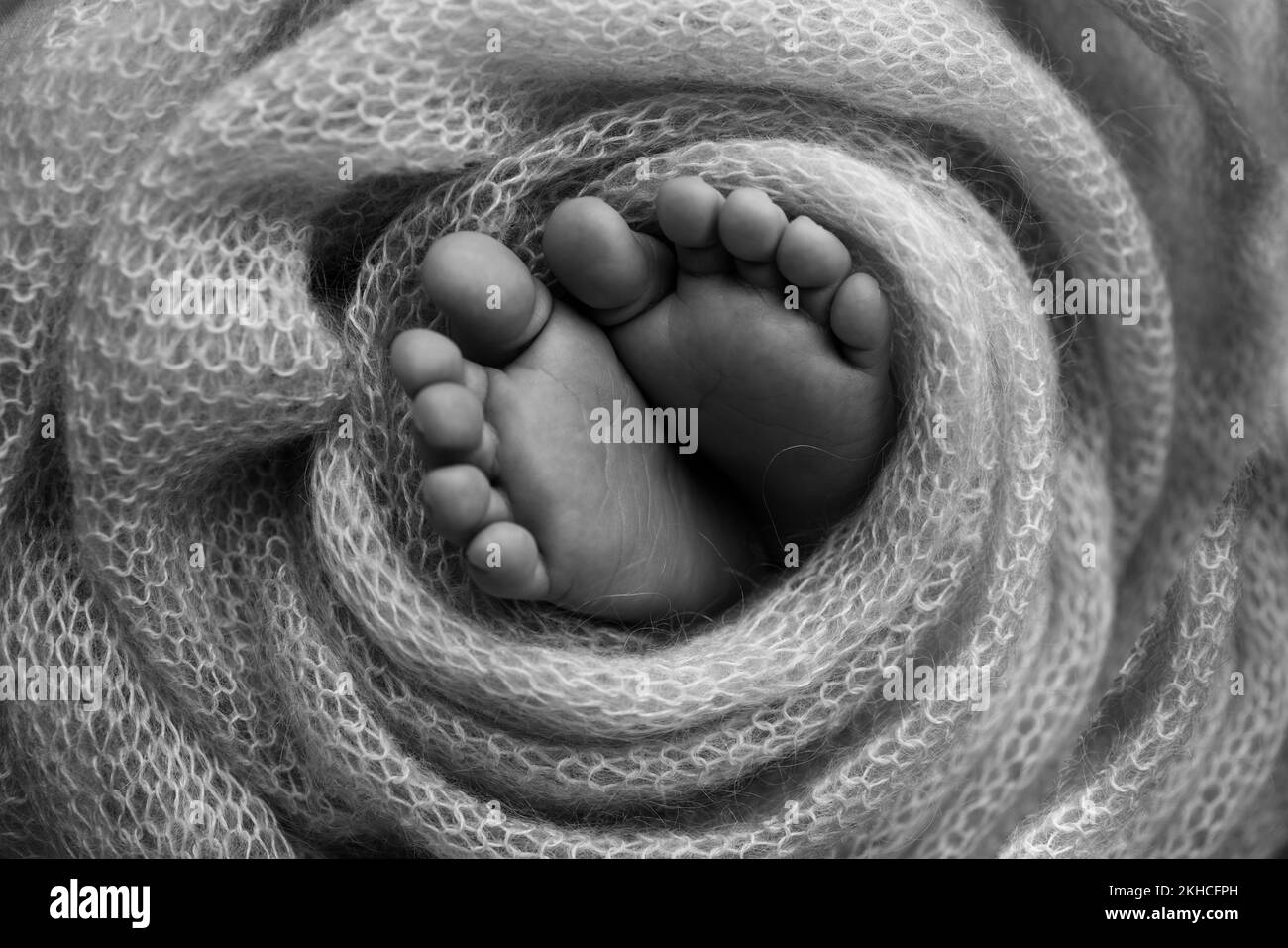 Weiche Füsse eines Neugeborenen in einer Wolldecke. Schwarzweiß-Makrofotografie. Stockfoto