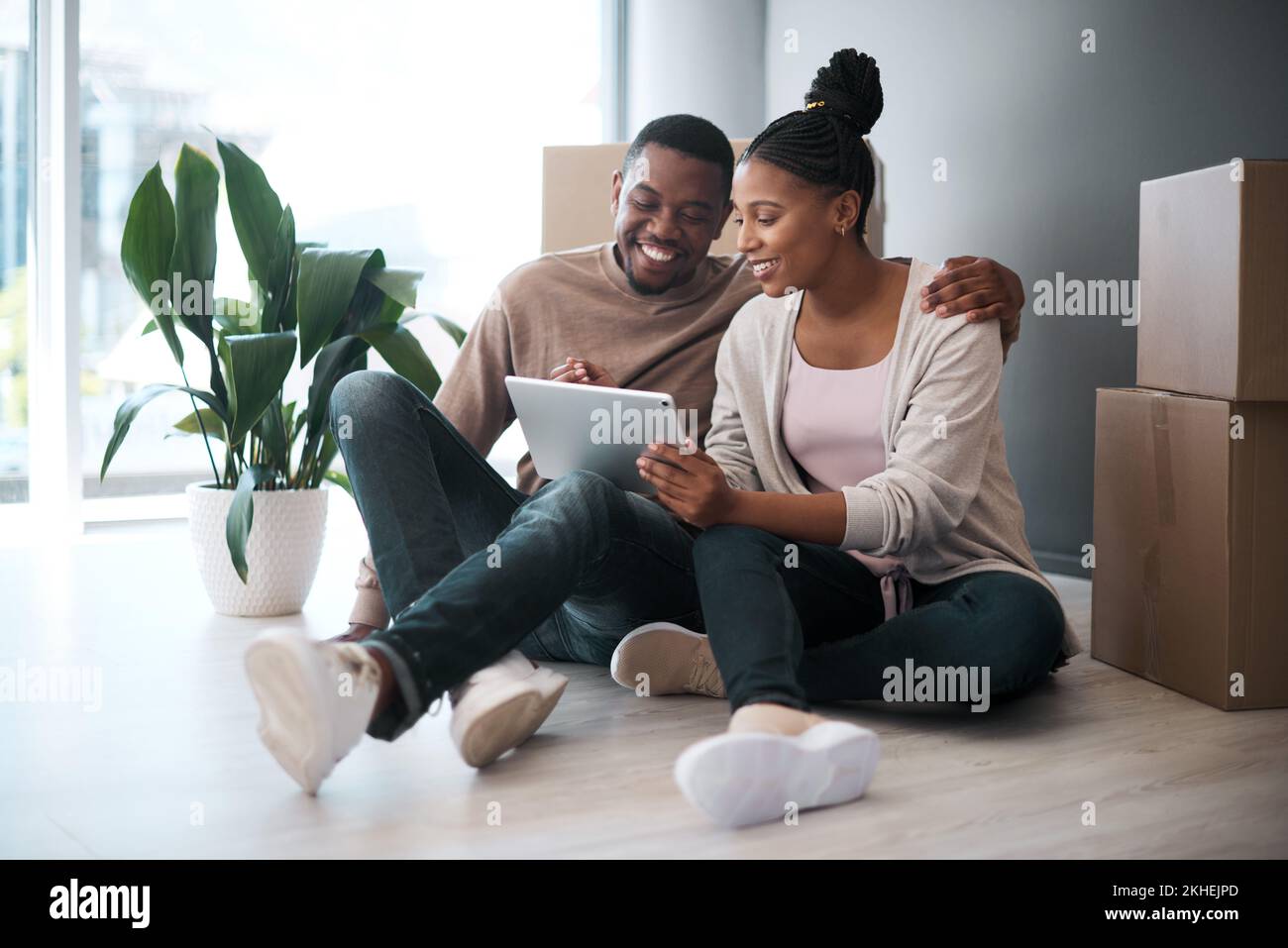 Afrikanisches Paar, Immobilien und Tablet für neue Hauseinkäufe, Anlage oder relaxen auf dem Boden mit Boxen. Makler, frohe Online-Kommunikation und Stockfoto