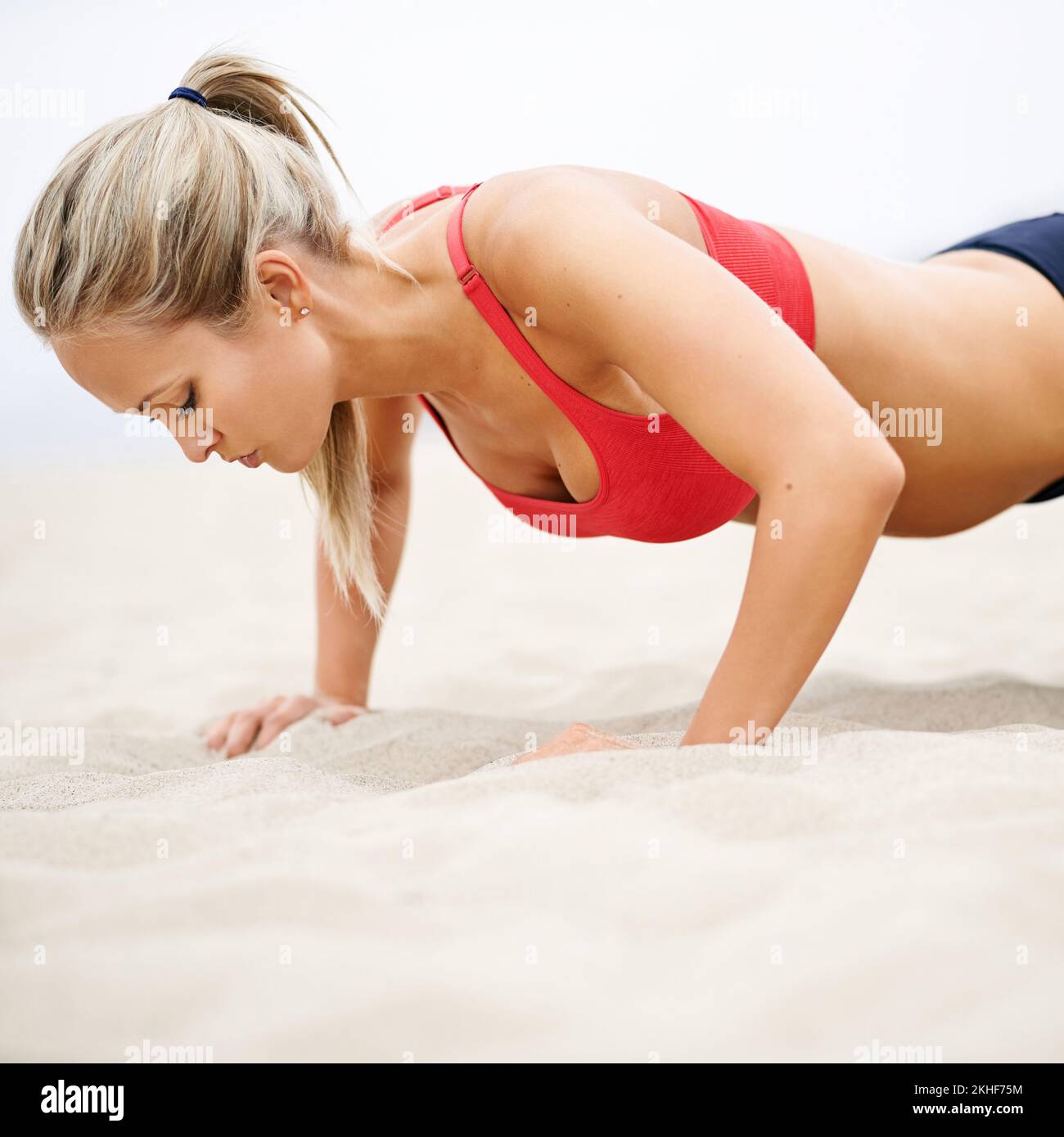Du gehst immer an deine Grenzen. Eine junge Frau in Sportkleidung, die Liegestütze am Strand macht. Stockfoto