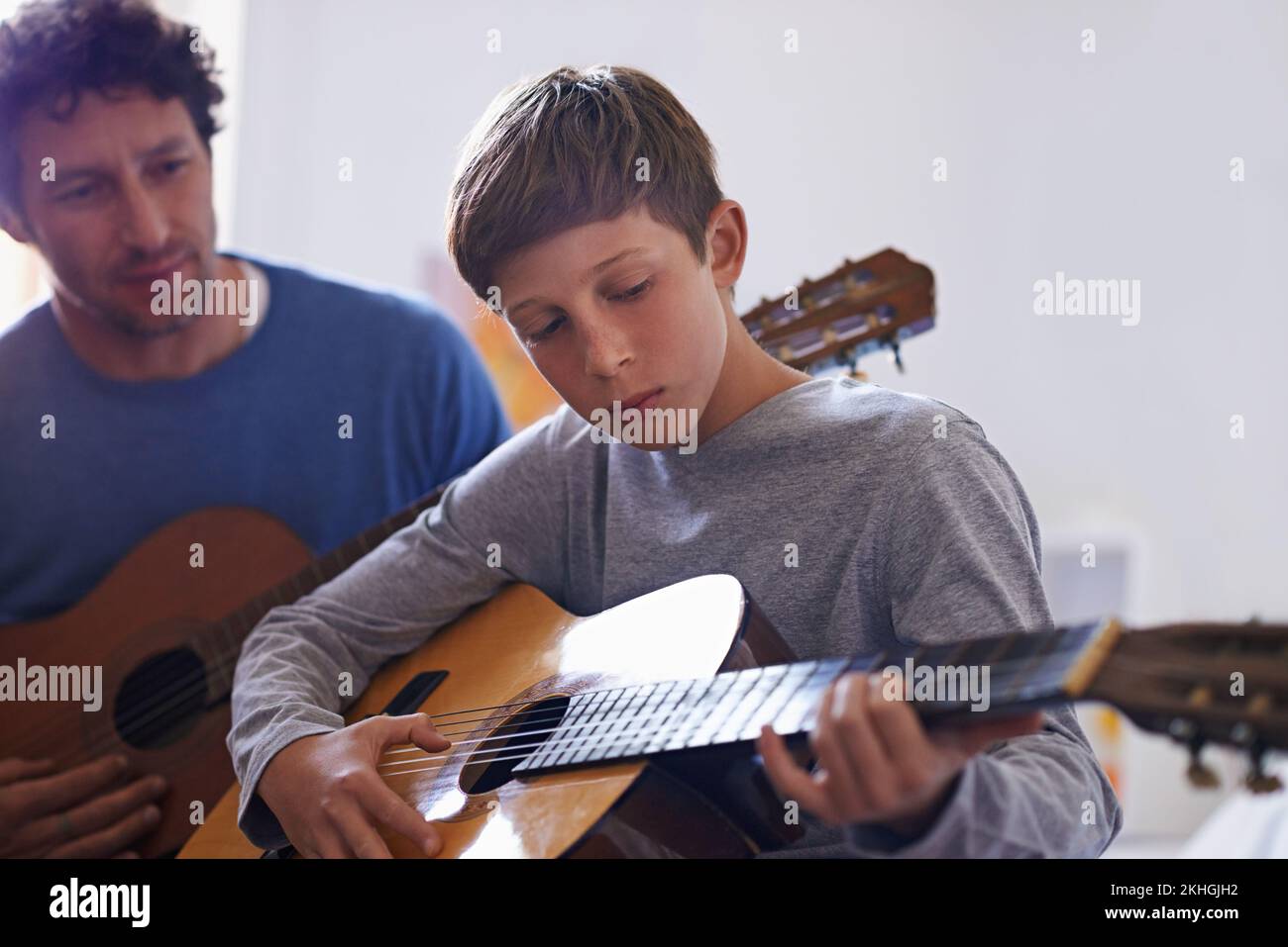 Die Fertigkeiten weitergeben. Ein Junge, der Gitarre spielt, von seinem Vater. Stockfoto
