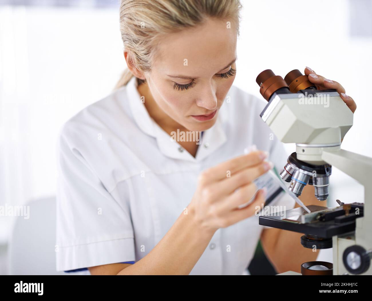 Es ist ernst damit, ein Heilmittel zu finden. Eine schöne Frau in einem Labor, die mit einem Mikroskop arbeitet. Stockfoto