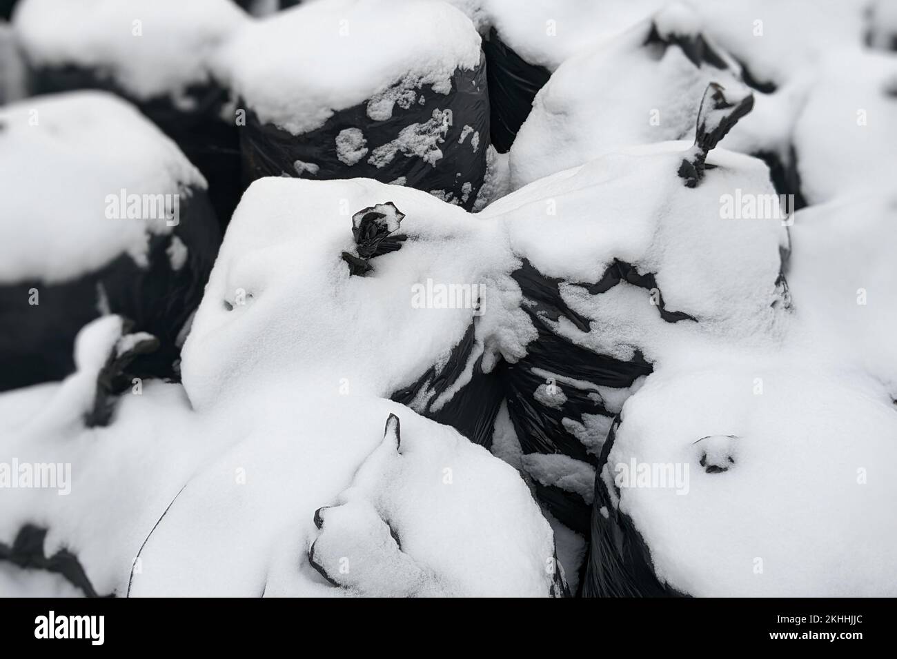 Ein Haufen voller schwarzer Müllsäcke im Freien unter Schnee. Große, dichte schwarze Müllsäcke mit gesammeltem Müll. Reinigung des Gebiets und der Umwelt von Stockfoto