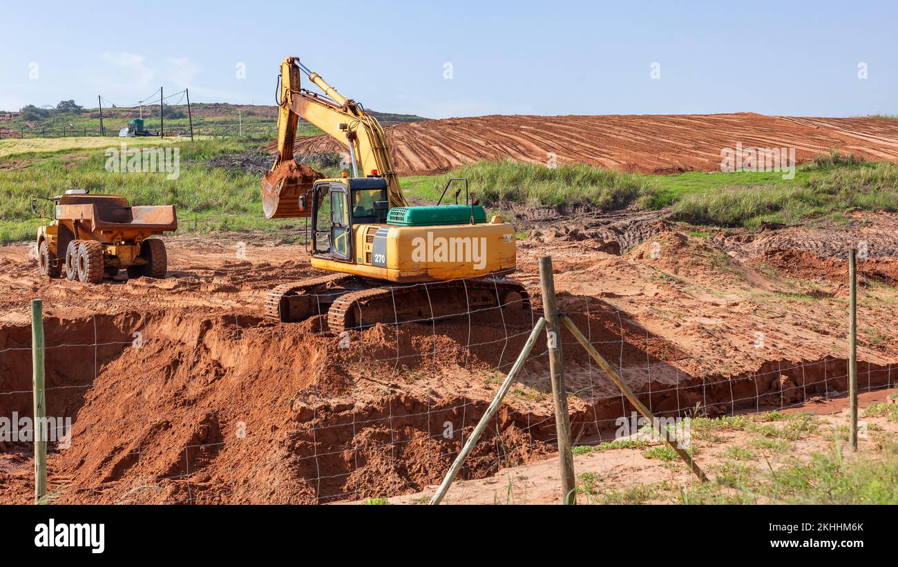 Schwerlastwagen für den Industriebau mit Baggermaschine, die Erdsand auf Plateau transportiert, um das Grundstückskonzept zu erweitern Stockfoto