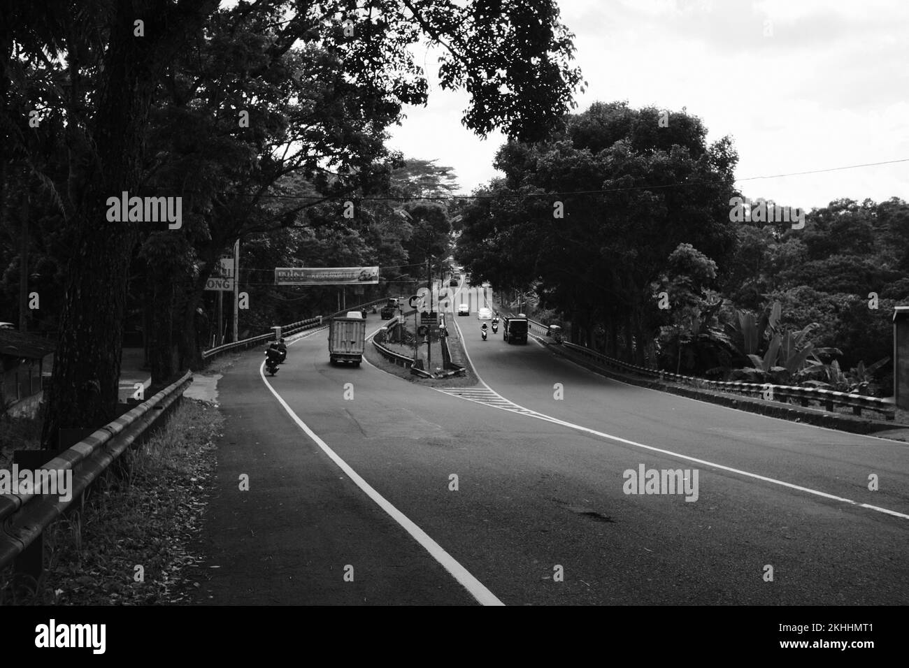 Schwarzweißfoto, Schwarzweißfoto einer verlassenen gewundenen Straße, die in Pangandaran - Indonesien selten von Fahrzeugen passiert wird Stockfoto