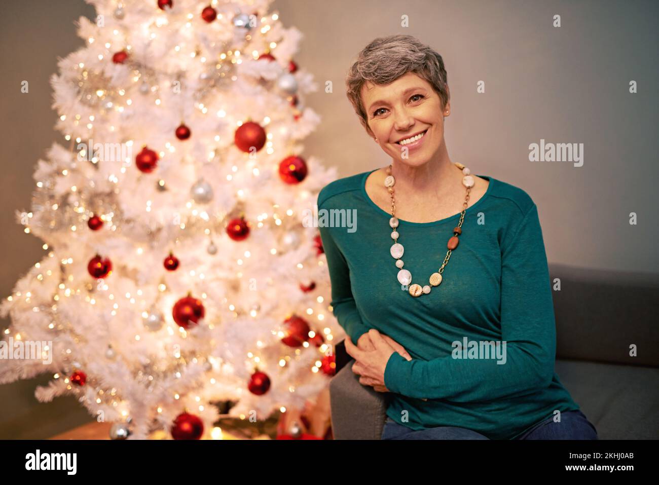 Träume von einem weißen Weihnachten. Ein Porträt einer glücklichen, reifen Frau, die neben einem weißen Weihnachtsbaum sitzt. Stockfoto