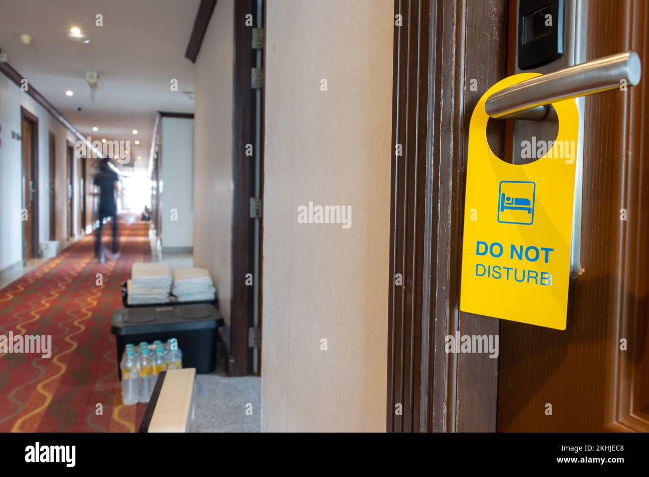 Das Schild „Bitte nicht stören“ hängt an der Türklinke des Hotelzimmers mit verschwommenen Personen auf einem Flur Stockfoto