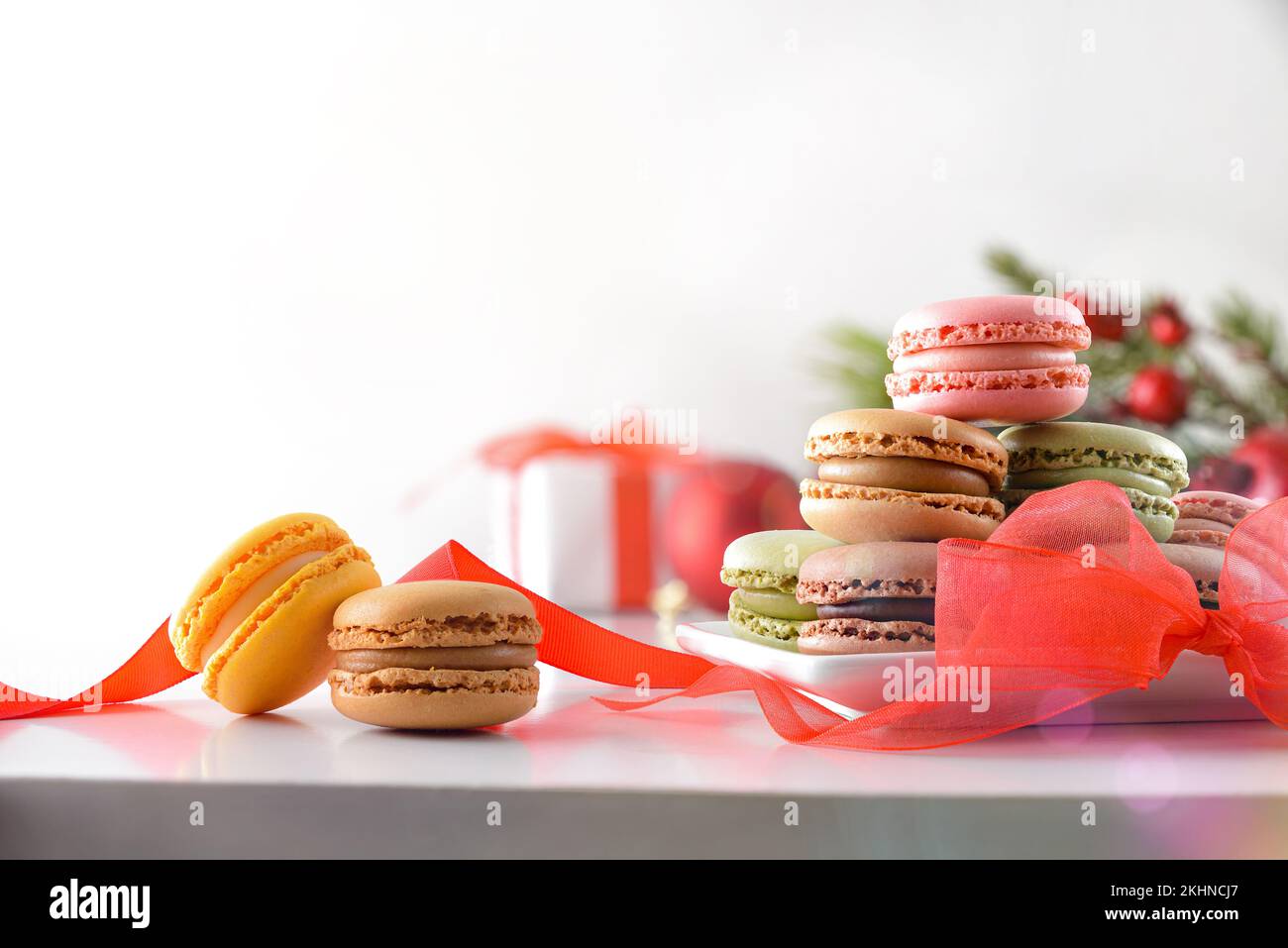Haufen französischer Makronen verschiedener Geschmacksrichtungen mit roter Schleife und Geschenk auf weißem isoliertem Hintergrund. Vorderansicht. Stockfoto