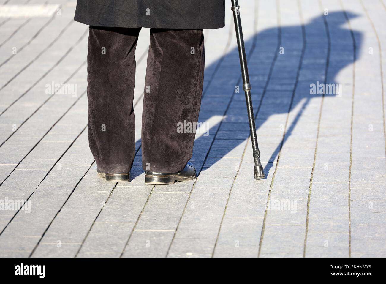 Hinkender Mann mit Gehstock, Schatten auf dem Gehweg. Konzept für Invalidität, Alter Stockfoto