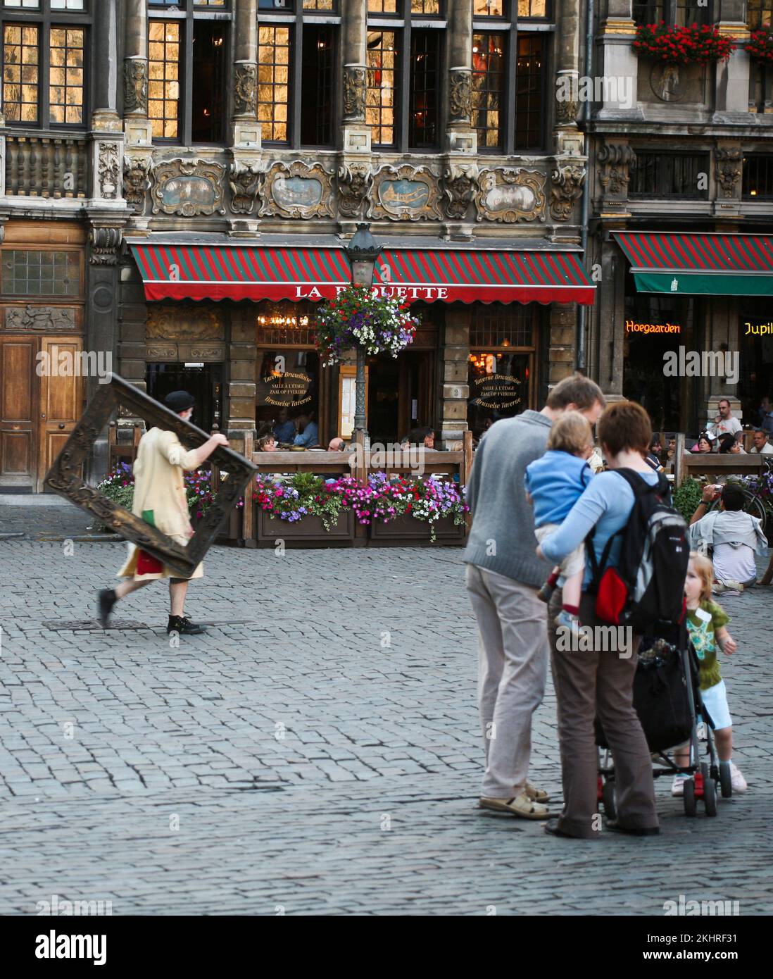 BRÜSSEL BELGIEN 2008 07 24Family mit Kindern im Gespräch, während ein Straßenkünstler mit seinem Bilderrahmen auf der Schulter über den Grand Place fährt Stockfoto