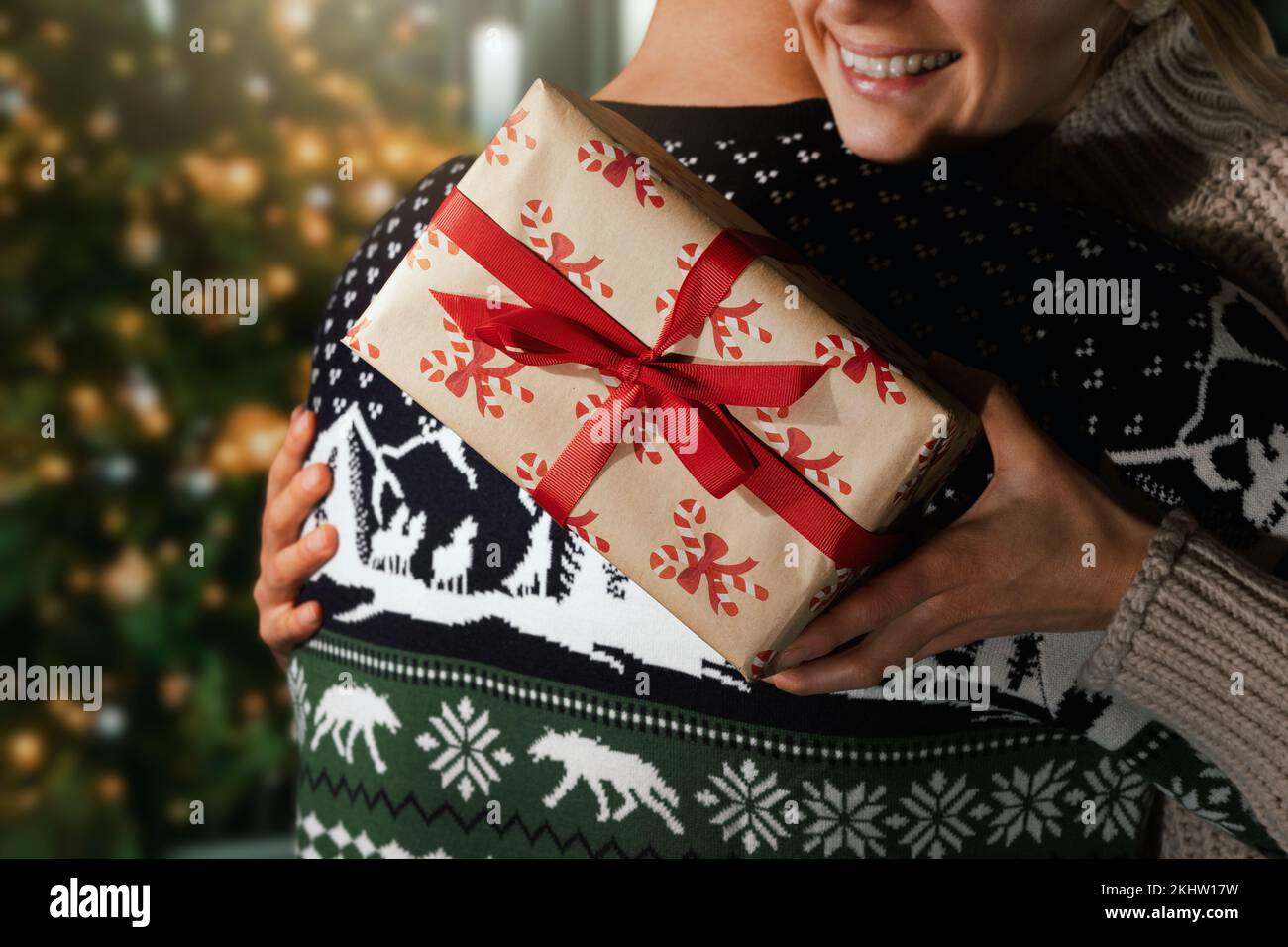 Frau umarmt ihren Mann neben dem weihnachtsbaum, nachdem sie zu Hause eine Geschenkbox erhalten hat Stockfoto