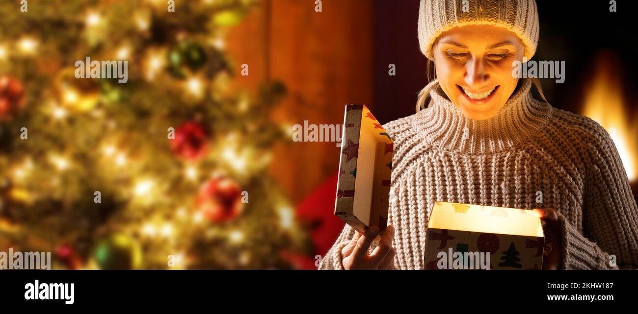 Glückliche Frau, die die weihnachtsgeschenkbox öffnet. Magisches Geschenk mit Licht im Inneren. Banner mit Kopierbereich Stockfoto