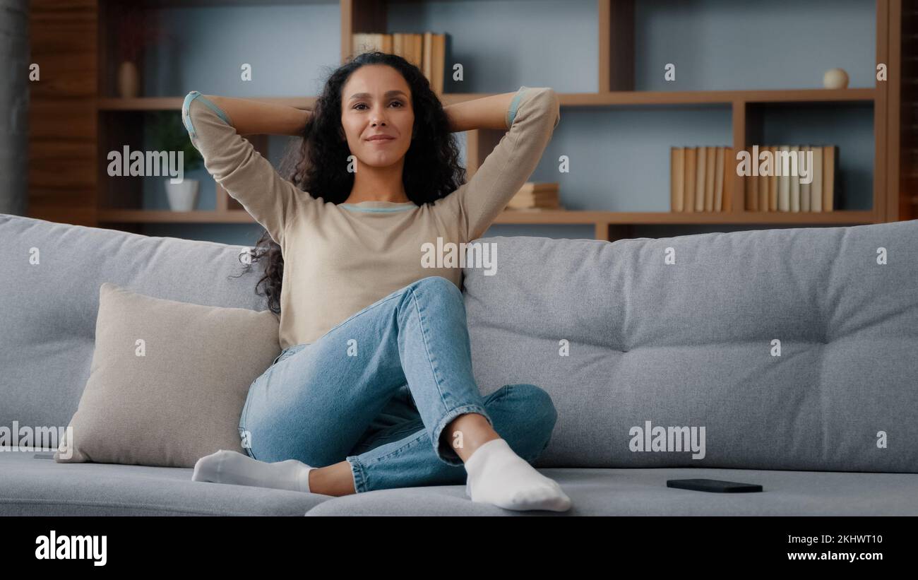 Ruhig glücklich in guter Stimmung Kaukasierin latino 30s Frau ruht sich auf der Couch neues Sofa im Wohnzimmer und streckt sich die Hände hinter dem Kopf gesunde Dame Stockfoto