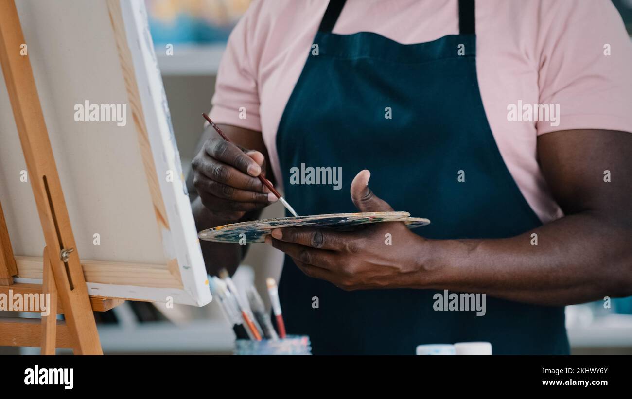 Nahaufnahme der männlichen Hände nicht erkennbarer afrikanischer Maler, der eine Palette mit hellen Öl-Acryl-Farben hält, Farben, auf denen Bilder erstellt werden Stockfoto