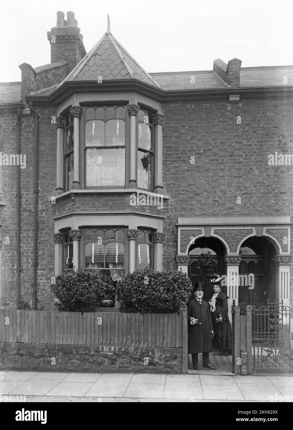 Ein spätes viktorianisches englisches Schwarzweißfoto, auf dem ein älterer Mann und eine ältere Frau in edler Kleidung vor ihrem Haus stehen. Stockfoto