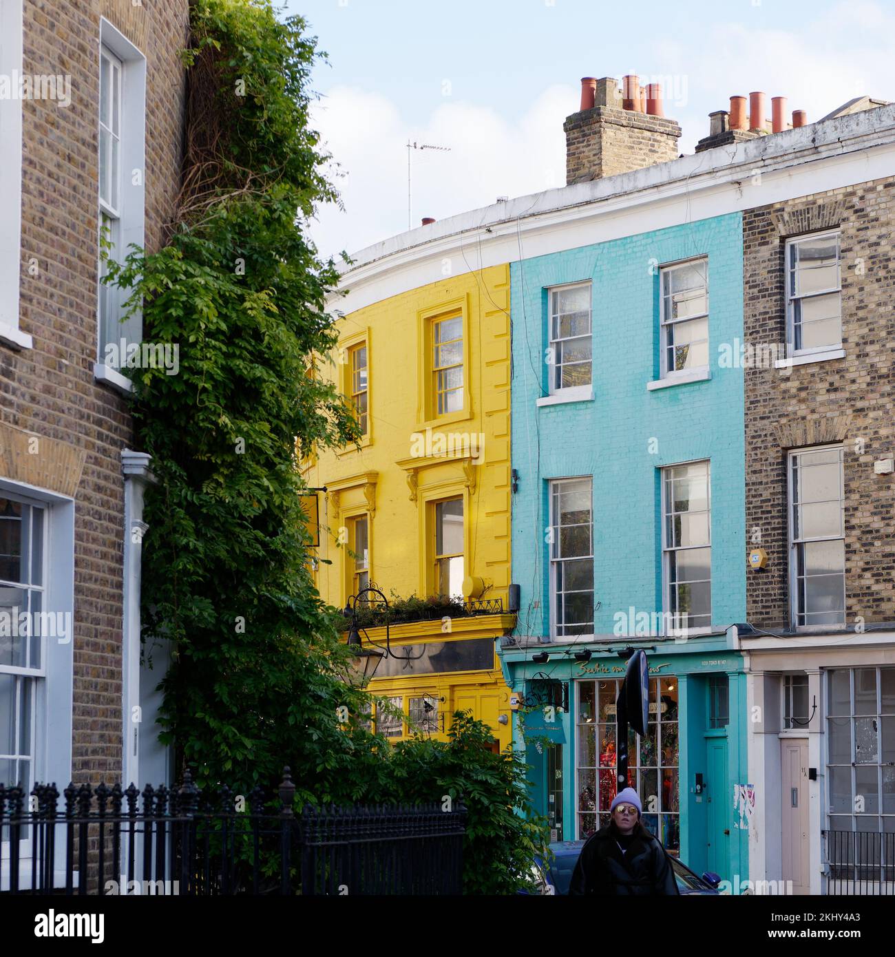 Gelbes und blaues Grundstück an der berühmten Portabello Road in der Notting Hill Gegend von London. Eine Dame mit einem lilafarbenen Wackelmütze im Vordergrund. Stockfoto