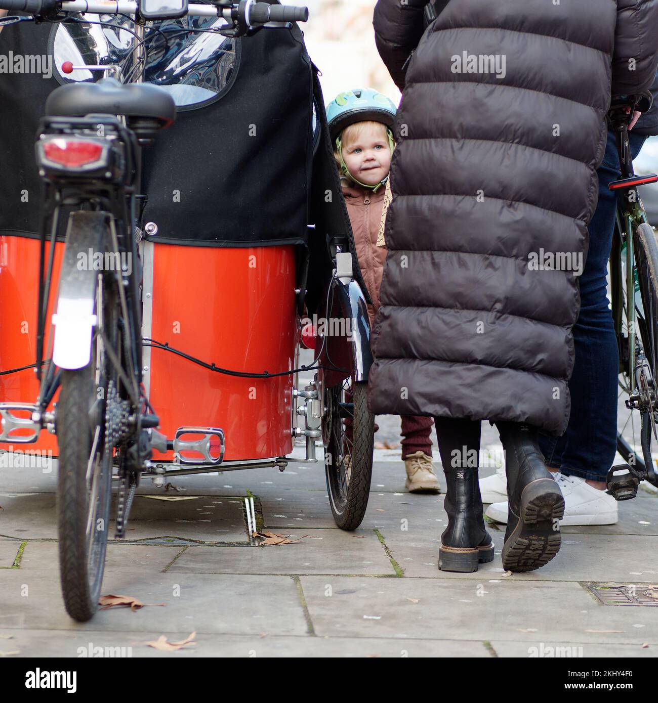 Kleines Kind, das einen Helm neben einem Dreirad mit Regenschutz trägt Stockfoto