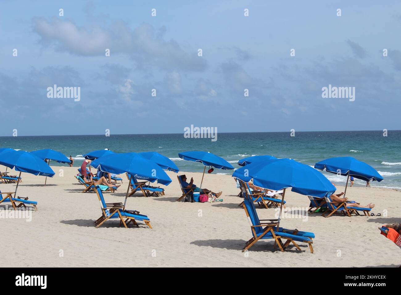 Delray Beach mit blauen Liegestühlen und Sonnenschirmen, blauem Himmel und Wolken im Hintergrund. Stockfoto