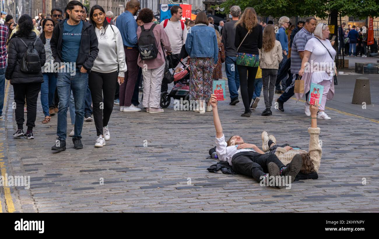 Bemannte Touristen umgehen die Künstler, die mitten in der Royal Mile in Edinburgh liegen und ihre Fringe Show „Bittersweet“ bewerben Stockfoto