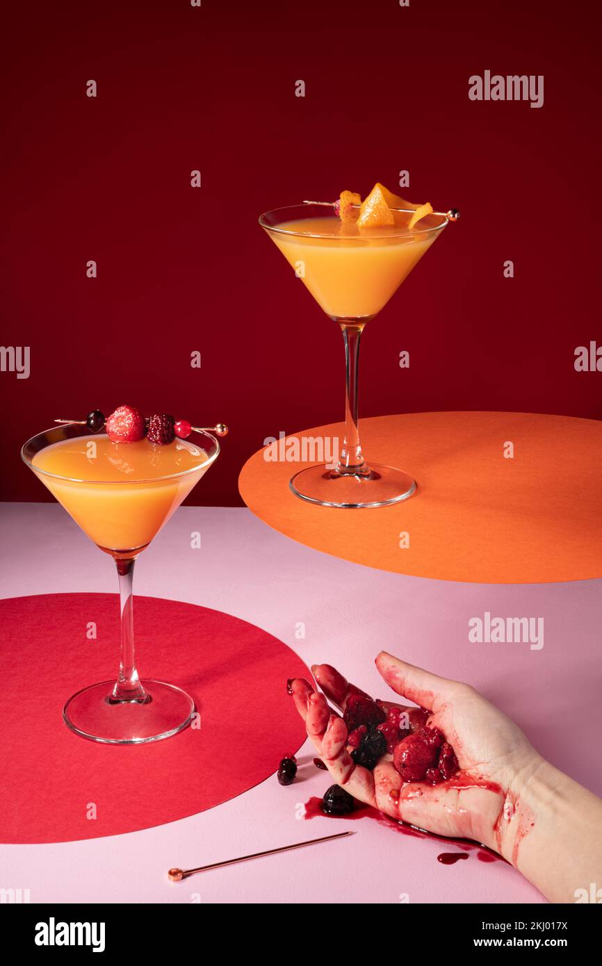 Szene mit der Hand einer betrunkenen Frau, die zerbrochene Beeren mit Orangensaft-Cocktails hielt. Moderne, lebendige Farben. Stockfoto