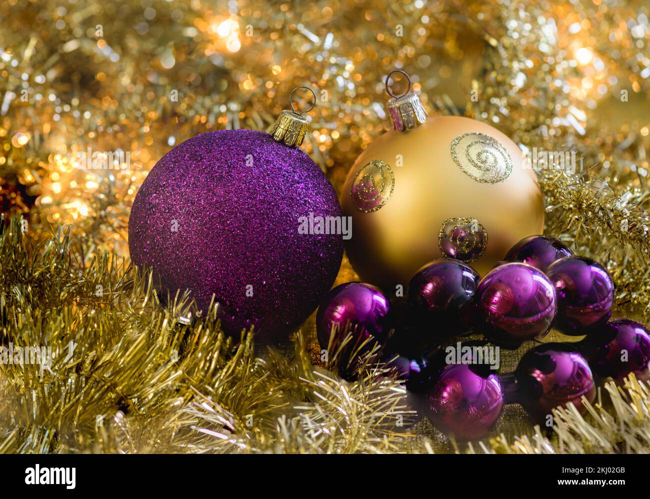 Lila und goldene weihnachtskugeln mit goldenen Girlanden und leuchtenden weihnachtslichtern im Hintergrund. Stockfoto