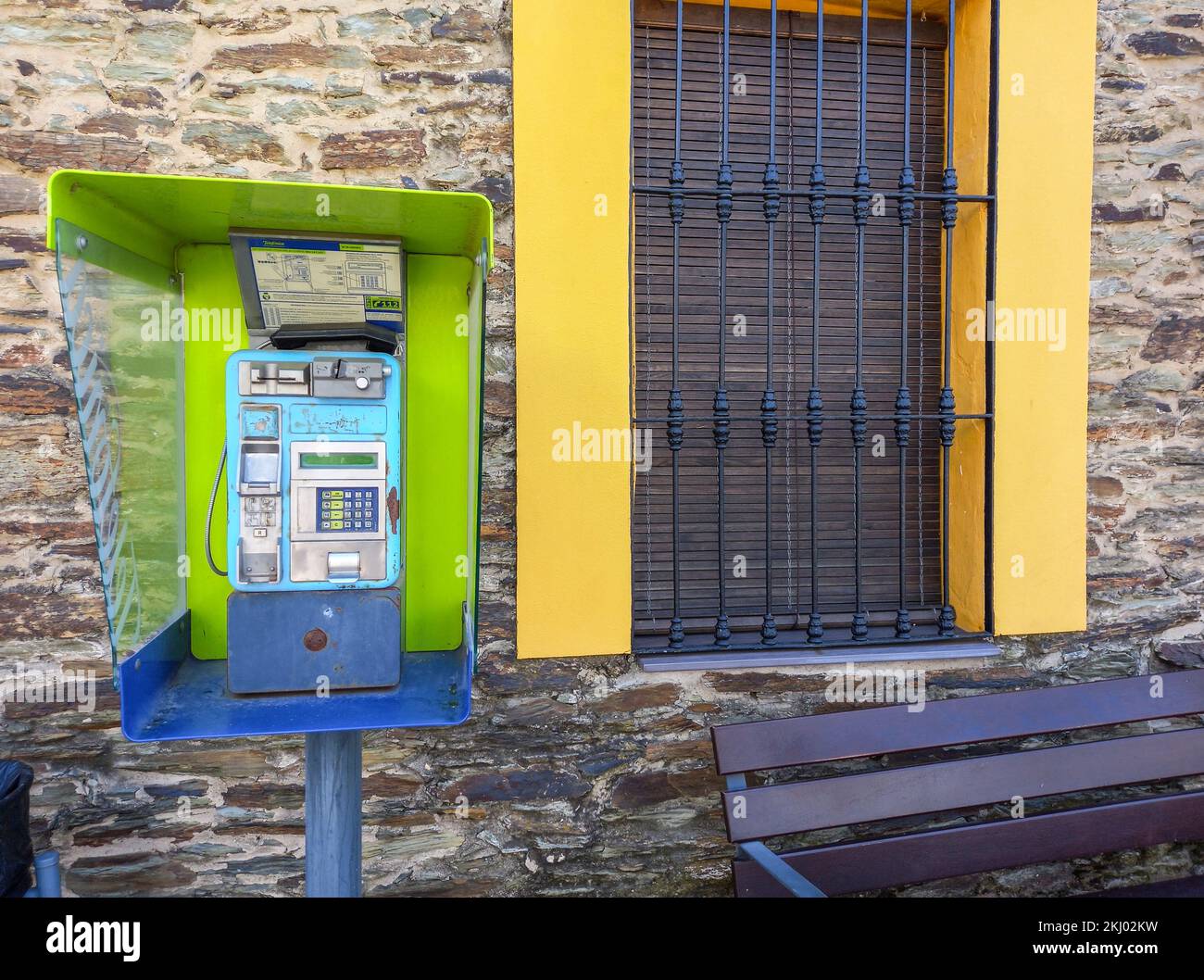 La Codosera, Badajoz - 19.. August 2021: Nicht geschlossene Telefonzelle in ländlichen Gebieten. Bürgersteig mit öffentlicher Bank Stockfoto