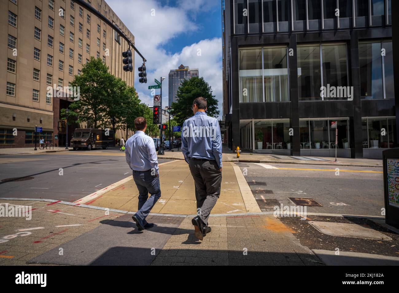 Geschäftsleute gehen mit den Händen in den Taschen zu einem Fußgängerüberweg, wo das Licht zwischen den Bürokomplexen rot ist Stockfoto