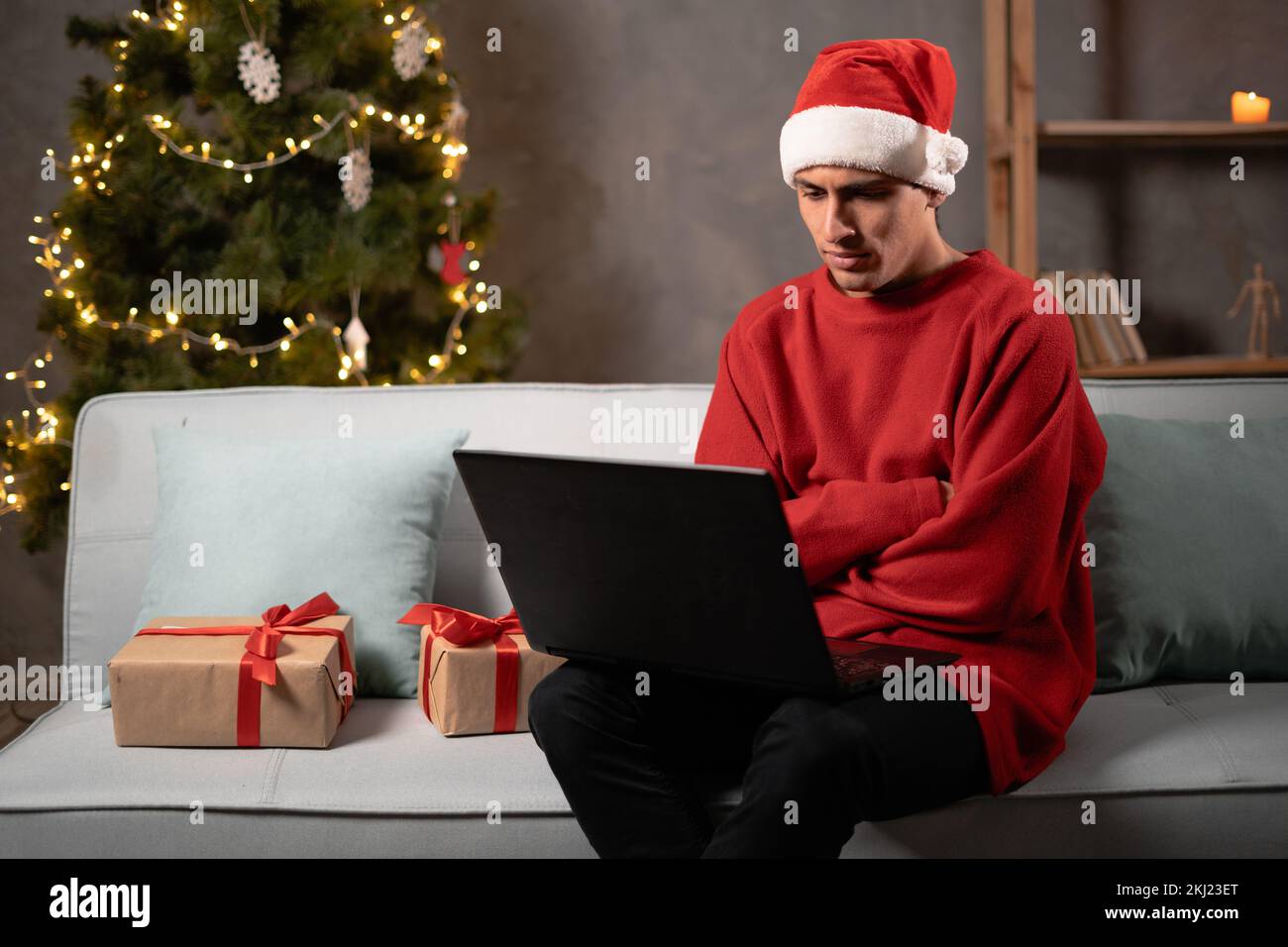 Ein arabischer Student mit weihnachtsmannmütze hat Probleme unzufrieden traurig zu Hause auf dem Sofa mit Laptop zu sitzen, unzufriedener Mann allein zu Hause. Speicherplatz kopieren Stockfoto