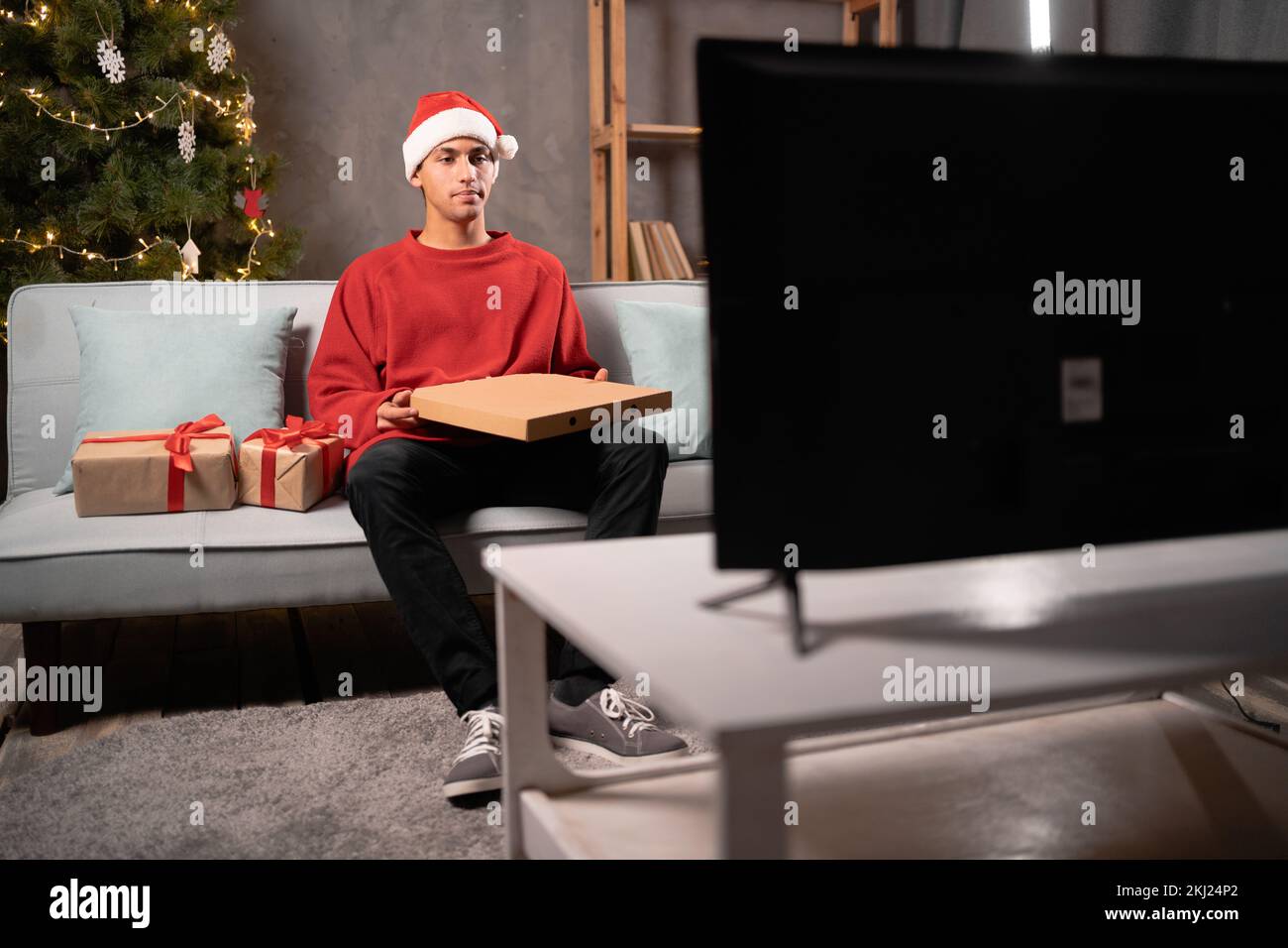 Ein junger arabischer Mann, der fernsieht und am weihnachtsabend frische Pizza isst. Speicherplatz kopieren Stockfoto