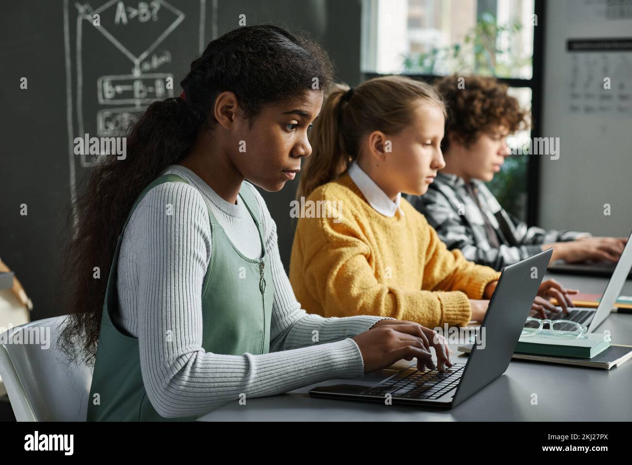 Eine Gruppe von Kindern, die am Schreibtisch hintereinander sitzen und mit neuer Software auf Computern in der Klasse arbeiten Stockfoto