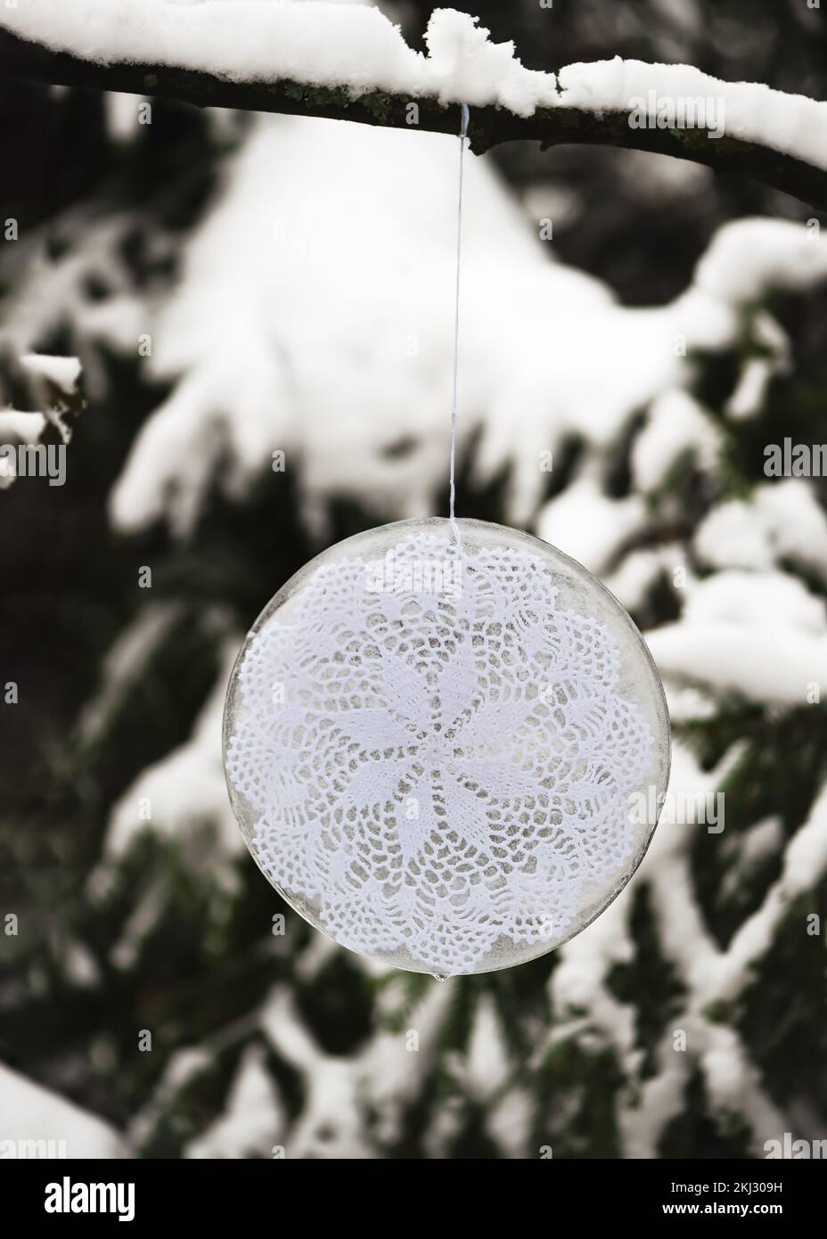 Winterdekoration im Freien aus Eis mit weißer gestrickter Serviette, die draußen in einem Wintergarten mit verschneitem Schnee am Ast eines Baumes hängt. Selektiver Fokus. Stockfoto