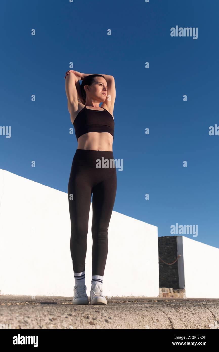 Sportliche Frau, die sich die Arme dehnt und sich aufwärmt. Fitnesskonzept im Freien. Stockfoto