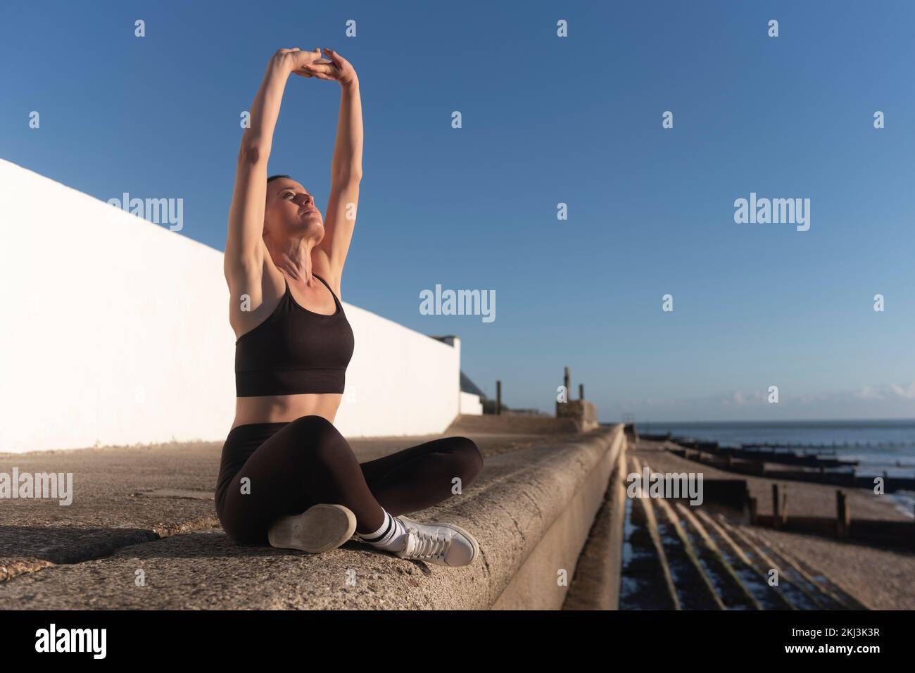 Eine Frau, die am Meer sitzt, Sport macht und sich streckt. Stockfoto