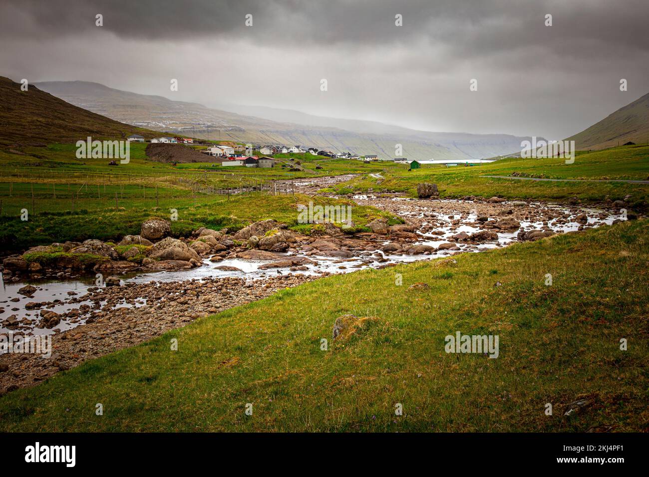 Fluss mit Steinen und Dorf im Hintergrund. Färöer. Stockfoto