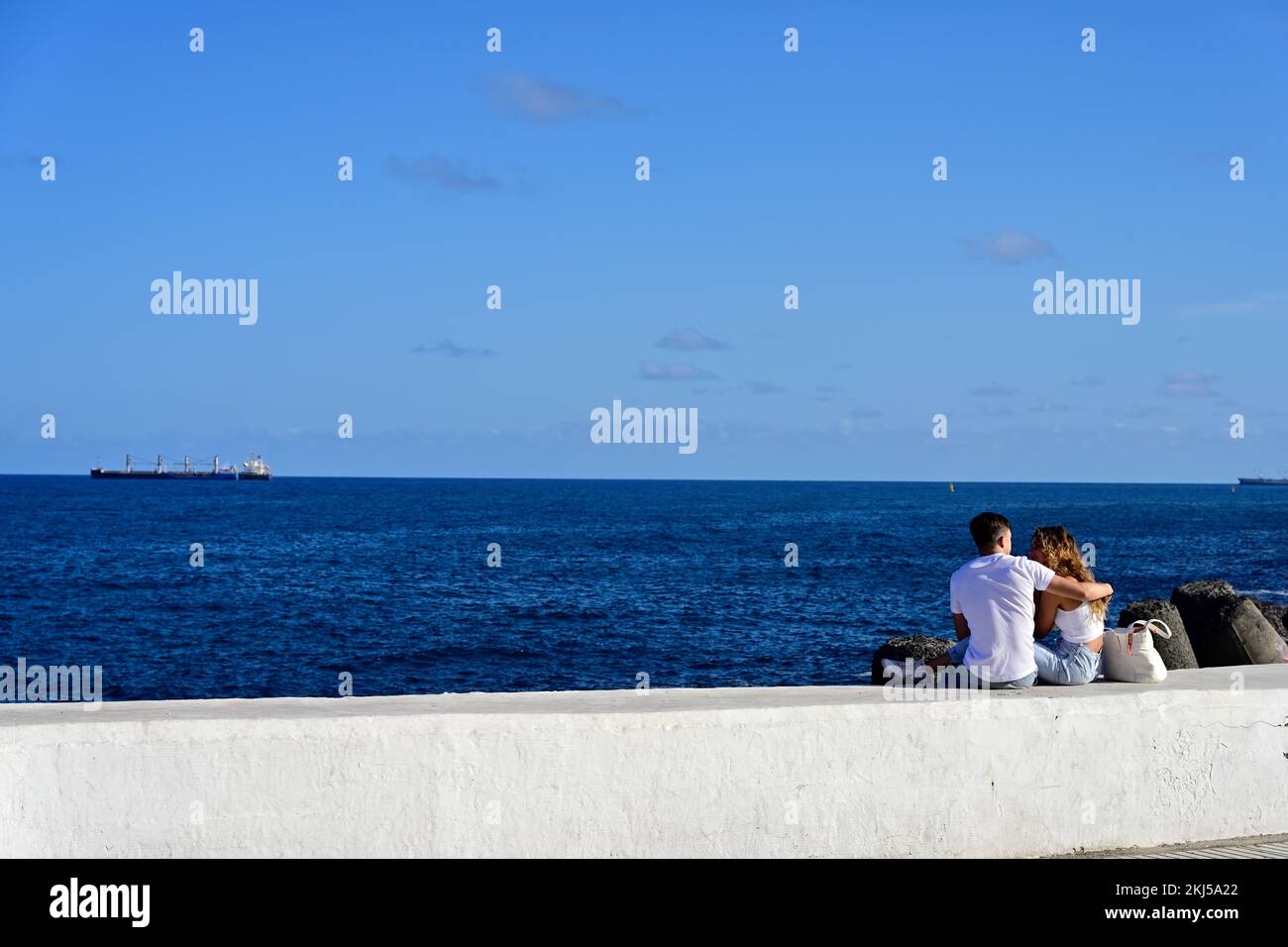 Ein junges romantisches Paar, das mit Schiffen an der Wand sitzt und den Atlantischen Ozean überblickt Stockfoto