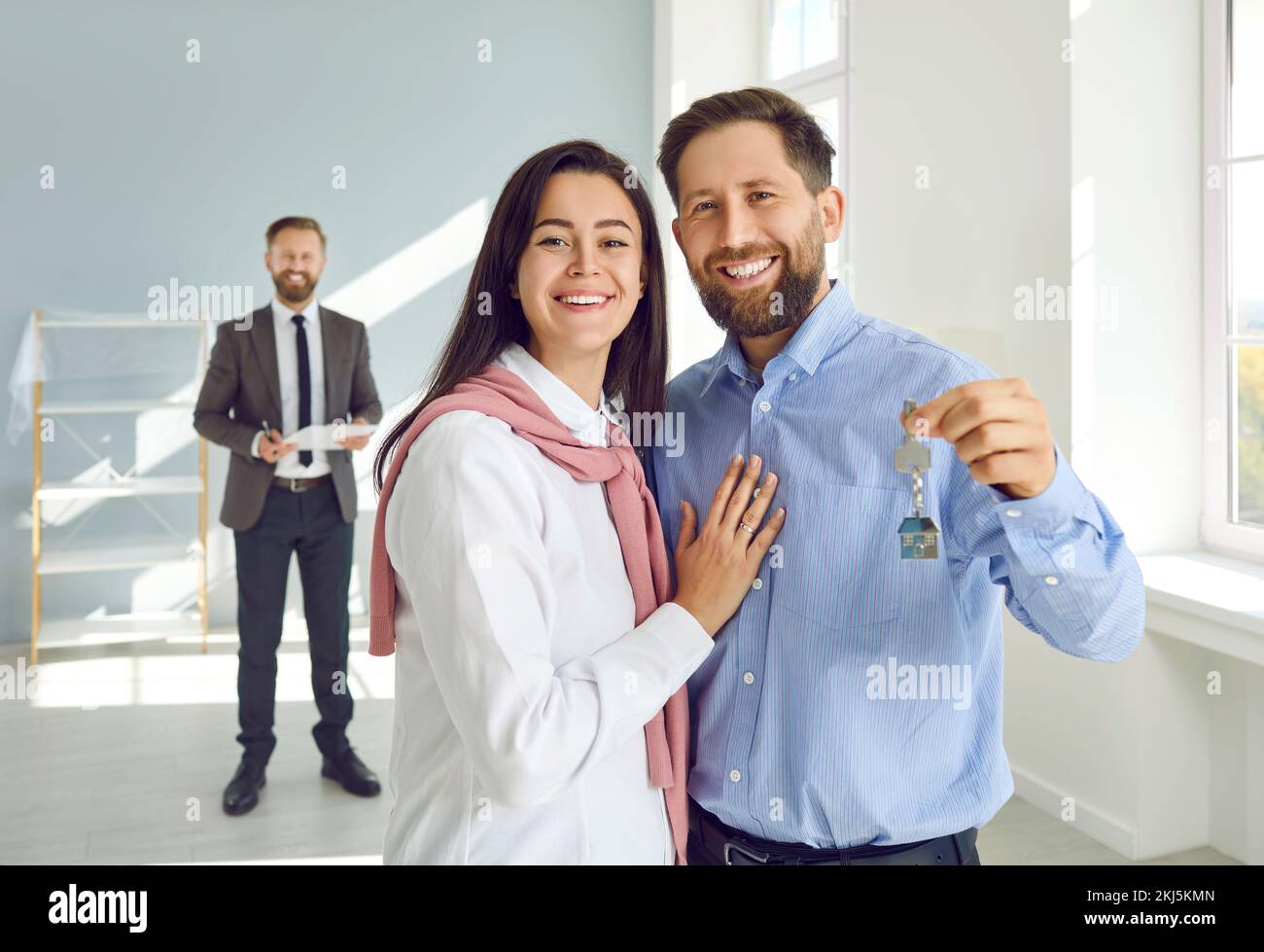 Porträt einer glücklichen jungen weißen Familie, die fröhlich und zufrieden Schlüssel zu ihrem neuen Zuhause zeigt. Stockfoto