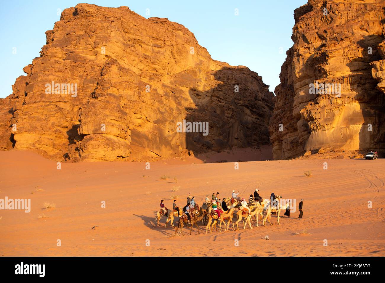 Jordanien, Wadi Rum - 2. November 2022: Kamelkarawane mit Touristen in der Wüste, Felsenberge bei Sonnenuntergang Stockfoto