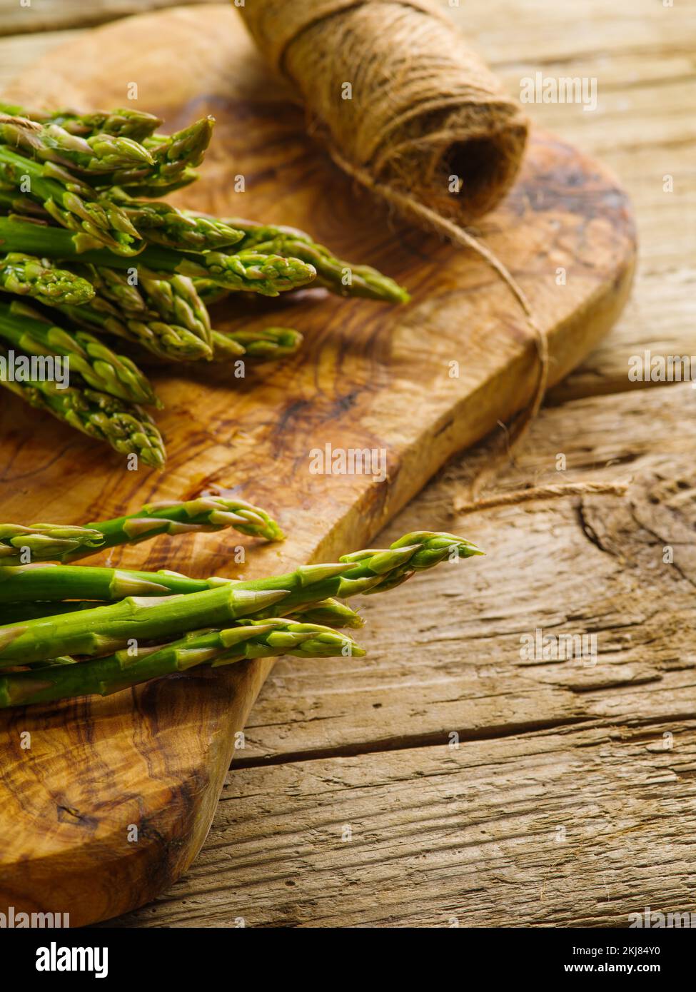 Viel frischer Spargel auf einem Schneidebrett. In der Nähe liegt ein Garnknüppel auf einem einfachen Holztisch. Kochen gesunder Gerichte mit Spargel. Rezepte, coo Stockfoto
