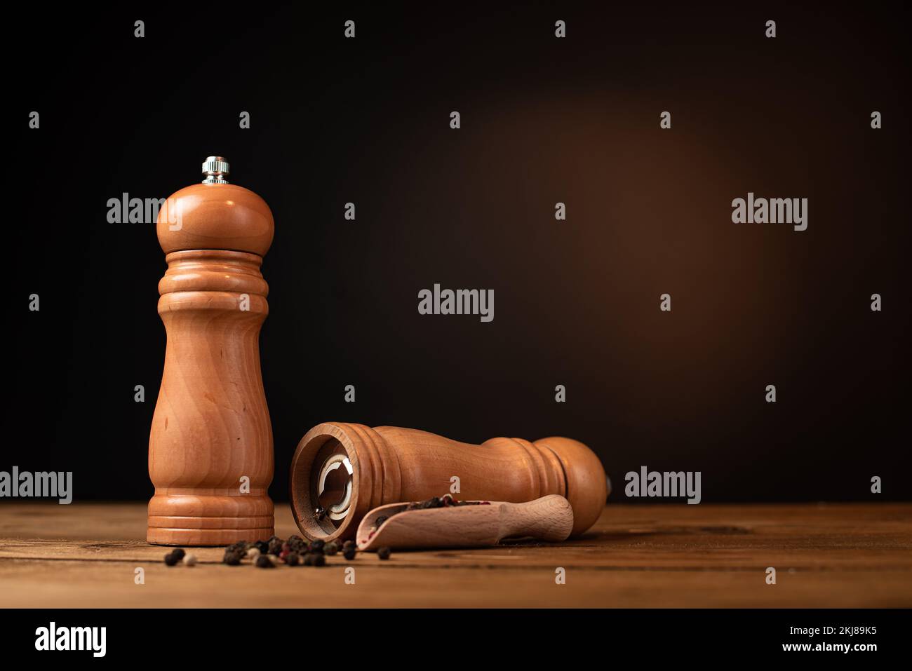 Pfeffermühle und ganzer Pfeffer in einer Holzschaufel auf einem Holztisch. Stockfoto