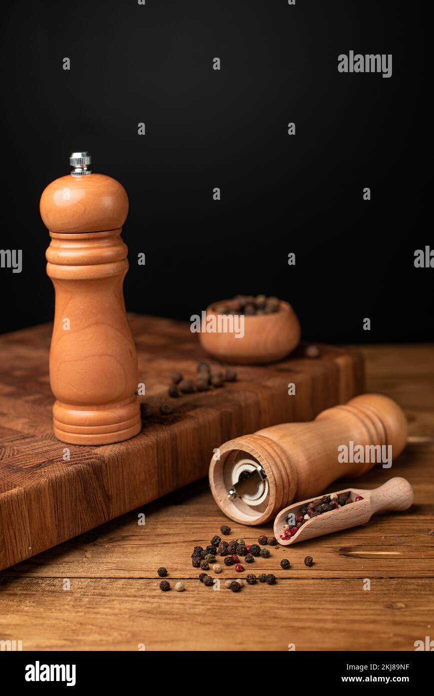 Pfeffermühle und ganzer Pfeffer in einer Holzschaufel auf einem Holztisch. Stockfoto