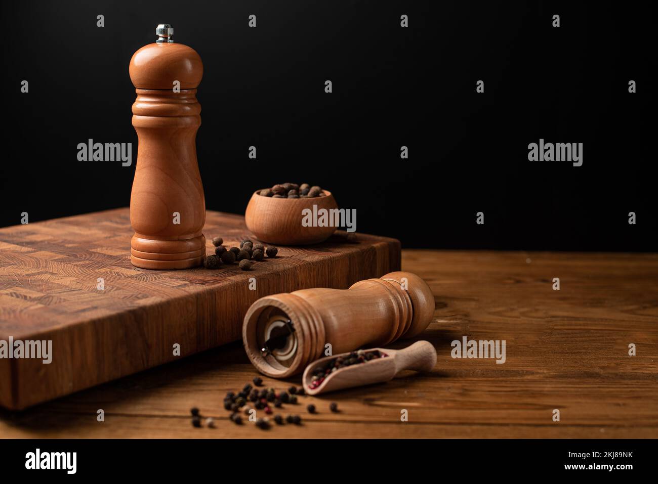 Pfeffermühle und ganzer Pfeffer in einer Holzschaufel auf einem Holztisch. Stockfoto