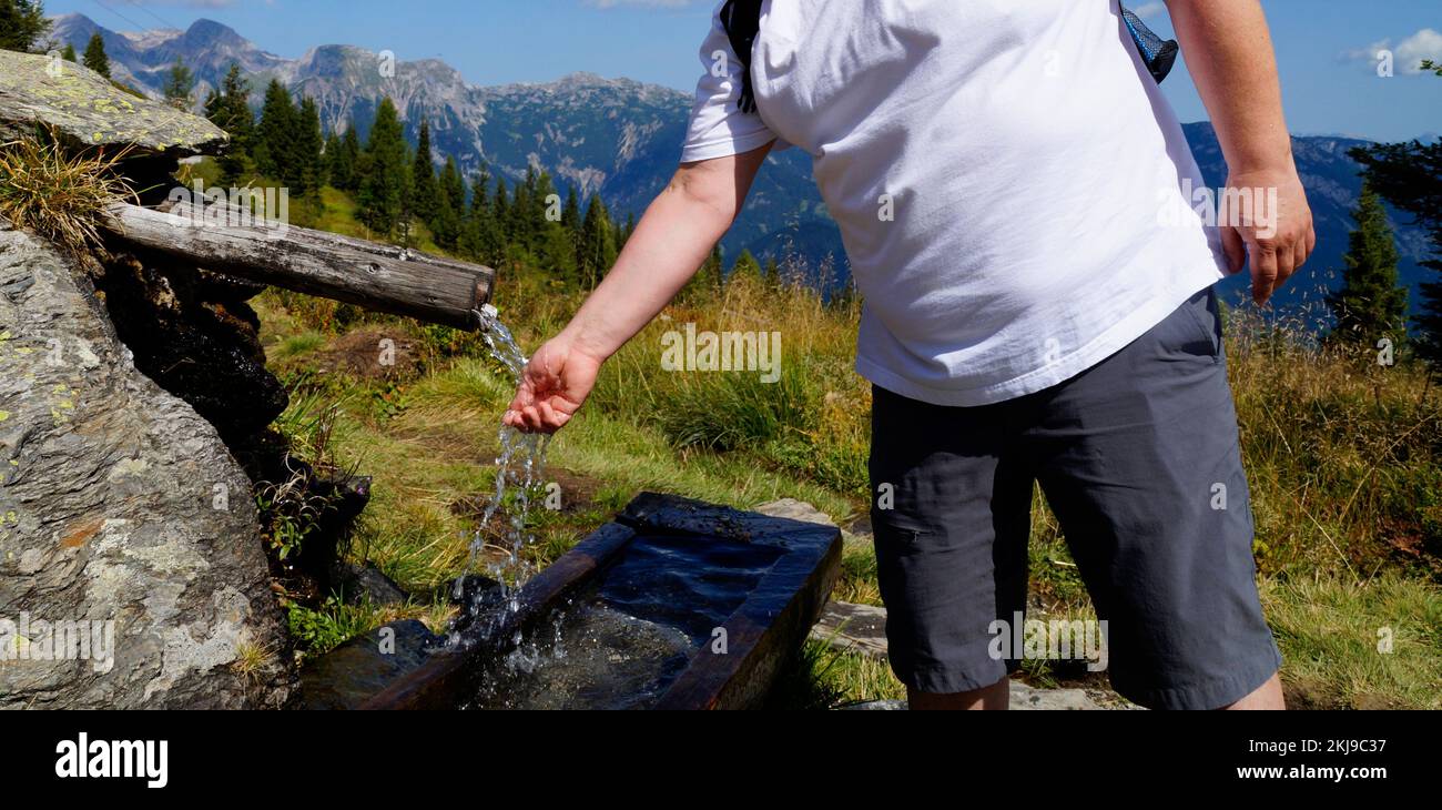 Ein Wanderer, der sich an einem heißen Tag am hölzernen Wassertrog mit sauberem eiskaltem Wasser in der Region Dachstein-Schladming in den österreichischen Alpen ausruht Stockfoto