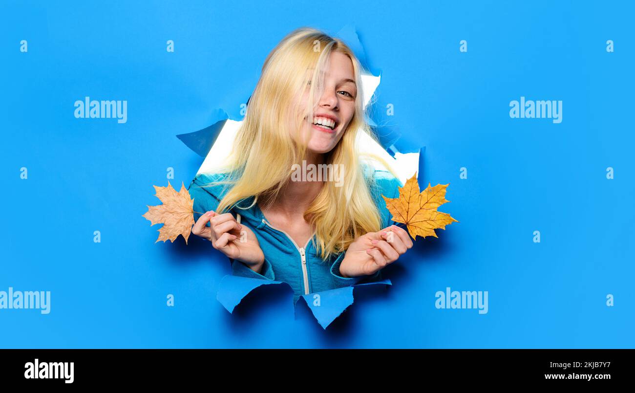 Lächelndes blondes Mädchen mit Ahornblättern, die durch das Loch schauen. Herbstverkäufe. Rabatt. Speicherplatz kopieren. Stockfoto