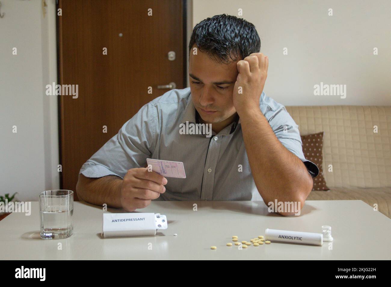 Besorgter Mann mit Führerschein in der Hand mit verschiedenen Anxiolytika und Antidepressiva-Pillen auf dem Tisch. Probleme und Nebenwirkungen bestimmter Arzneimittel Stockfoto