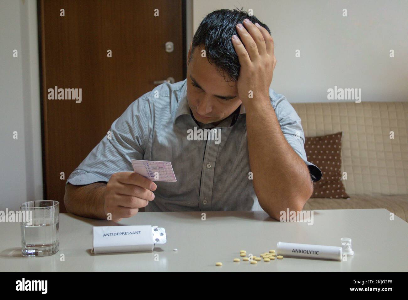 Besorgter Mann mit Hand im Haar, Führerschein mit Medikamenten wie Antidepressiva und Anxiolytika auf dem Tisch. Wirkung bestimmter Arzneimittel Stockfoto