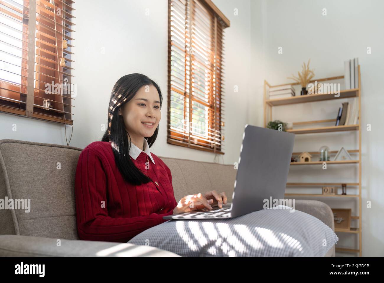 Junge asiatische Frau, die einen Laptop benutzt und im Wohnzimmer auf den Bildschirm schaut, Remote Job oder Arbeit von zu Hause Konzept. Stockfoto