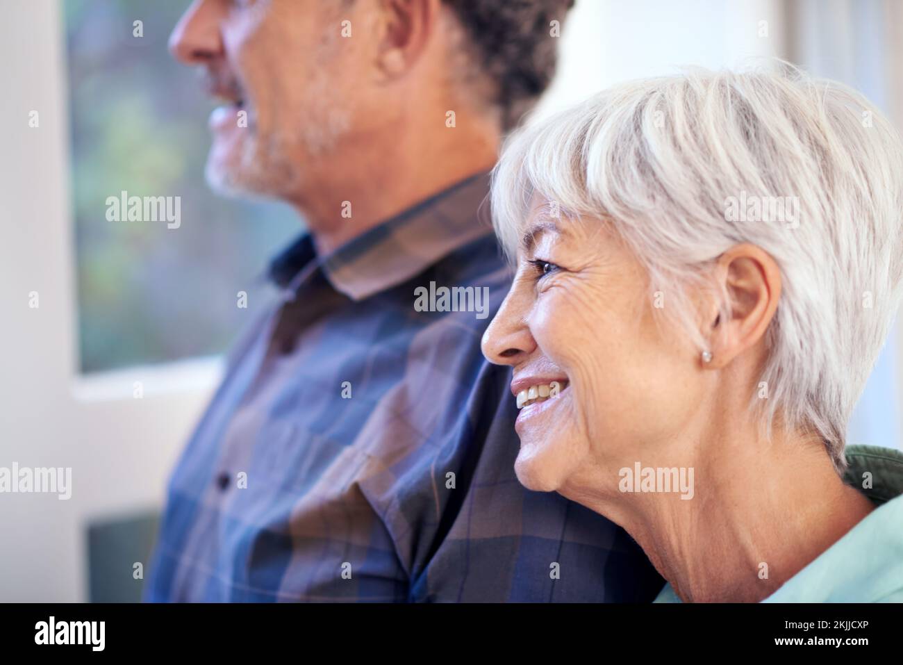 Es kommt noch viel mehr. Ein glückliches Seniorenpaar, das zusammen aus dem Fenster schaut. Stockfoto
