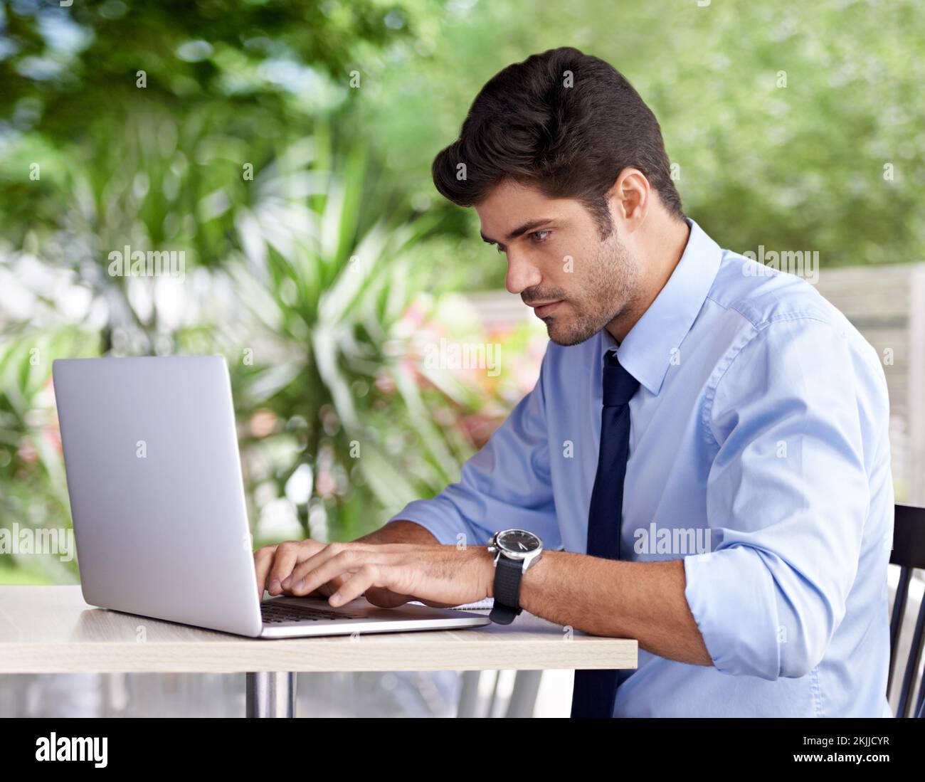 Er nimmt seine Arbeit überall hin mit. Ein gutaussehender junger Geschäftsmann, der draußen an seinem Laptop arbeitet. Stockfoto