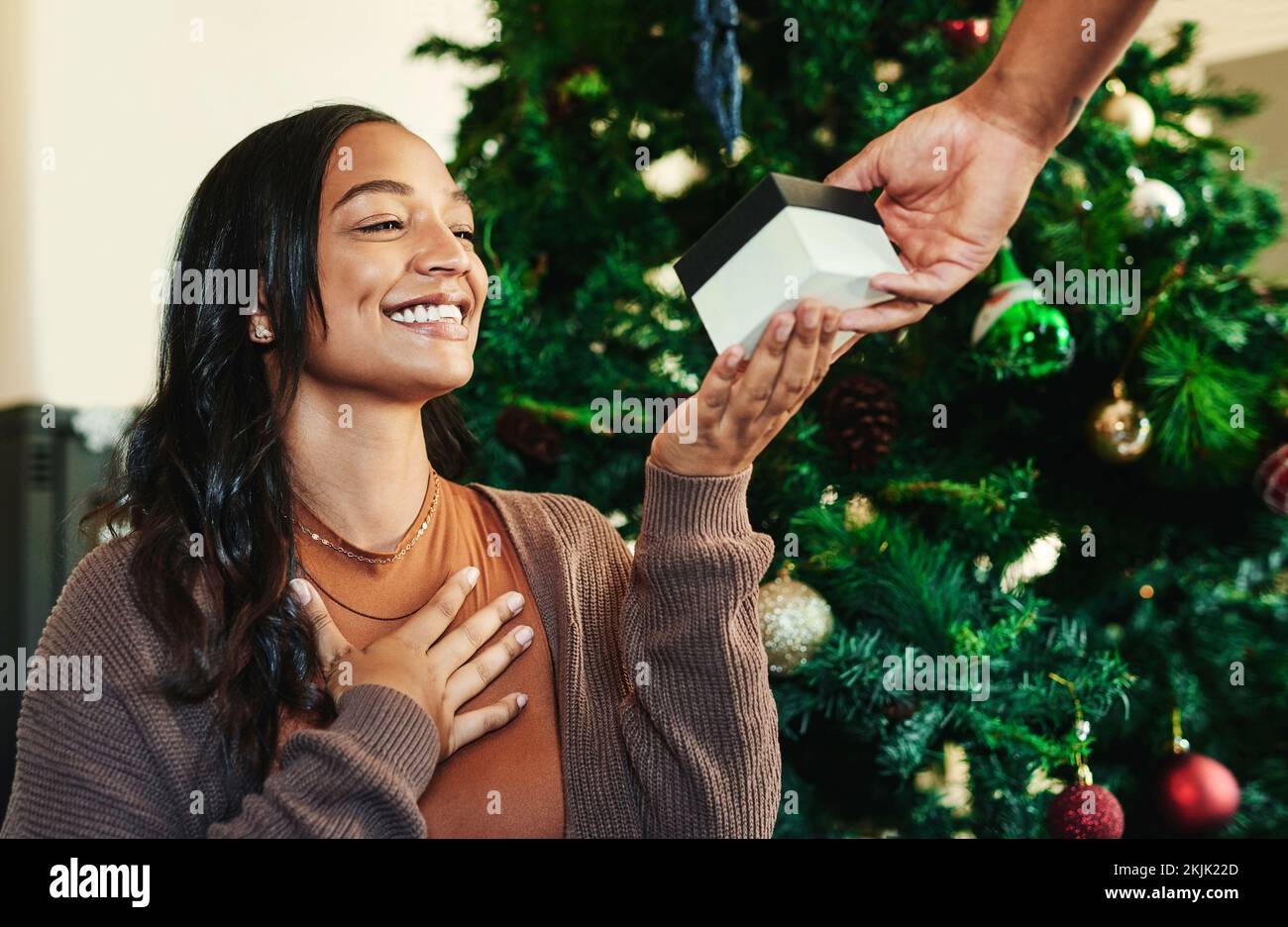 Weihnachten, Hand mit Geschenk und Frau mit Lächeln, Paar- und Geschenkaustausch, Überraschung und glücklich Feiertage zu feiern. Weihnachtsbaum, Liebe und Fürsorge Stockfoto