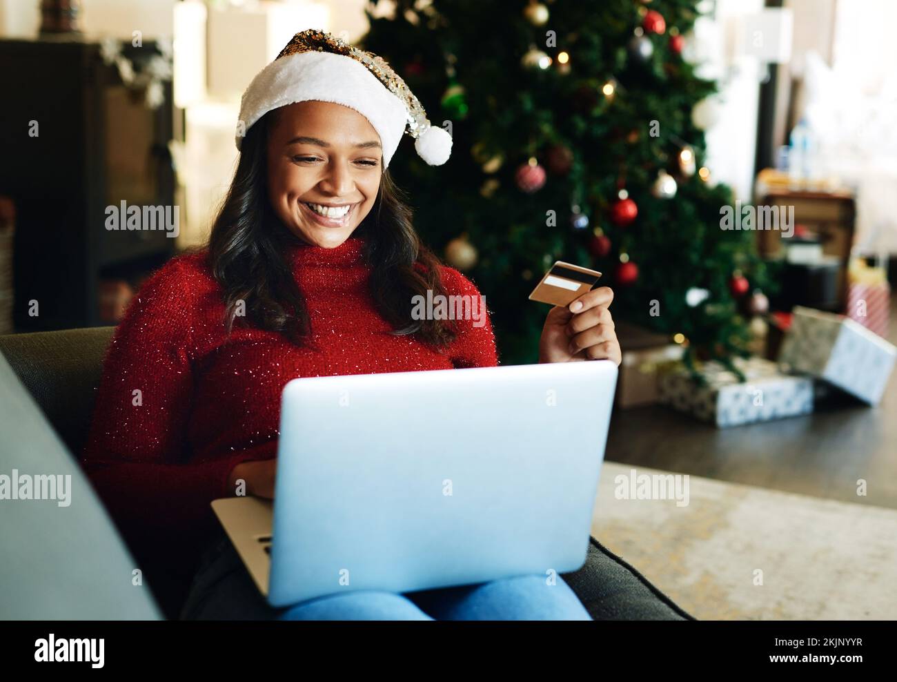 Kreditkarte, Laptop und Frau kaufen am Weihnachtstag online im Wohnzimmer ein. FinTech, Weihnachtsfeiertage und glückliche Frau aus Indien auf Computer, virtuell Stockfoto